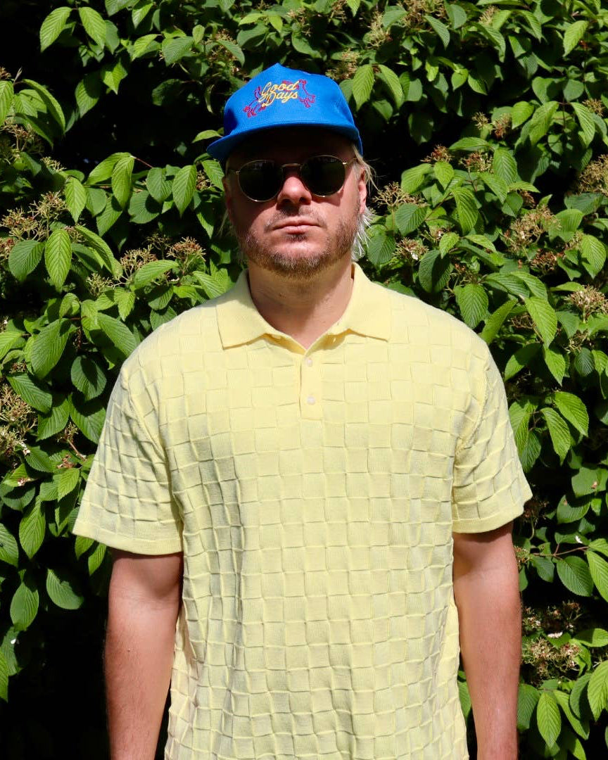 Man wearing a blue cap and yellow shirt standing in front of green foliage