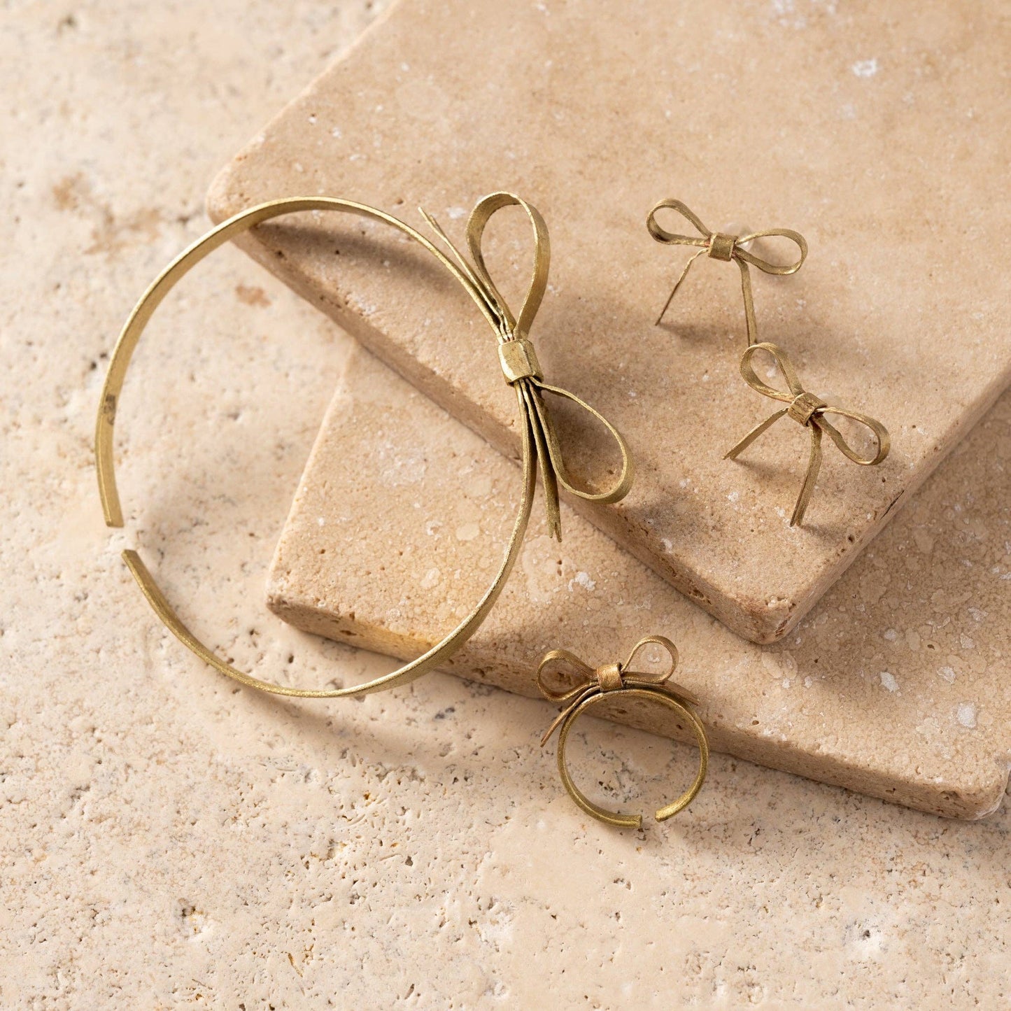 Gold bow-shaped jewelry on a beige stone surface