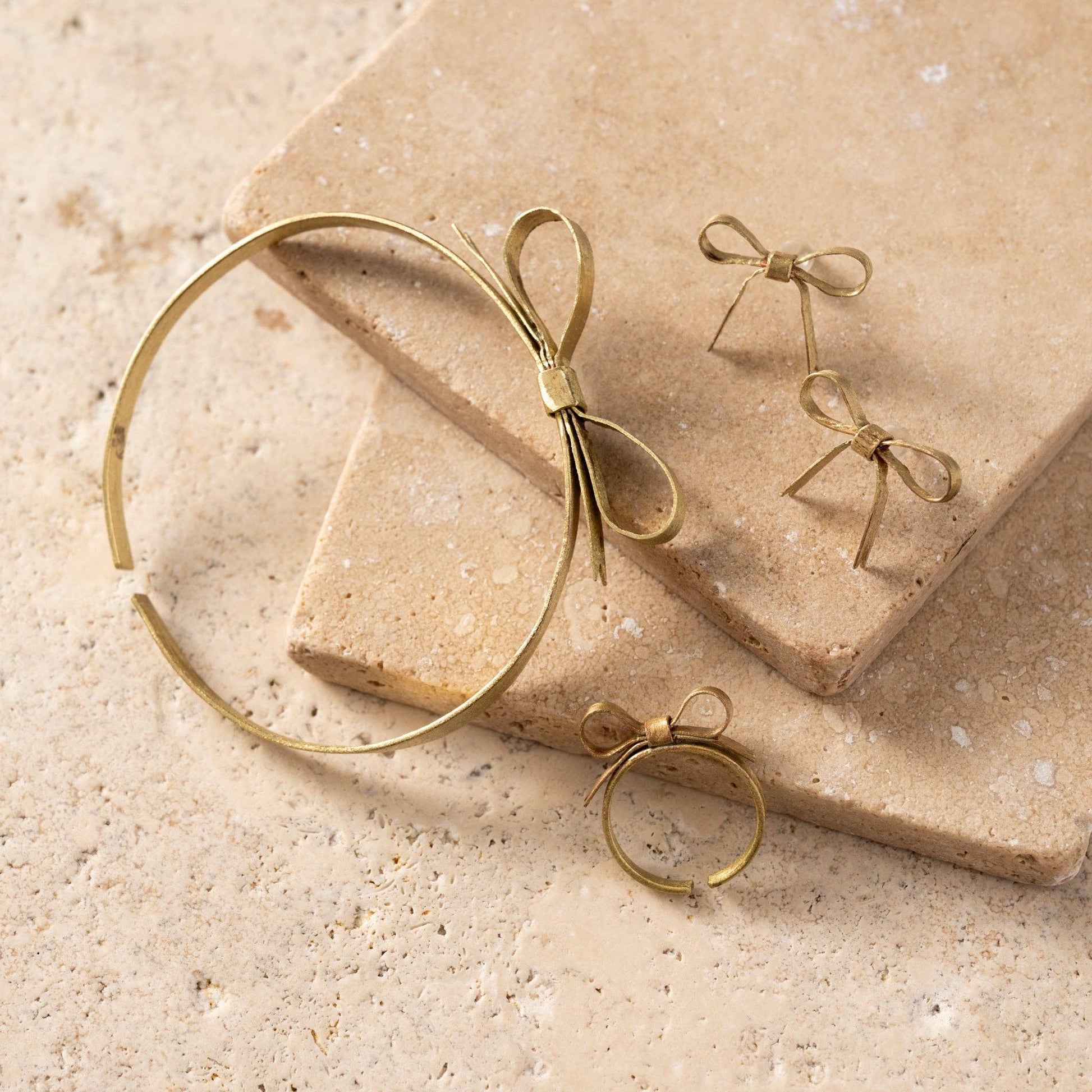Gold bow-shaped jewelry on a beige stone surface