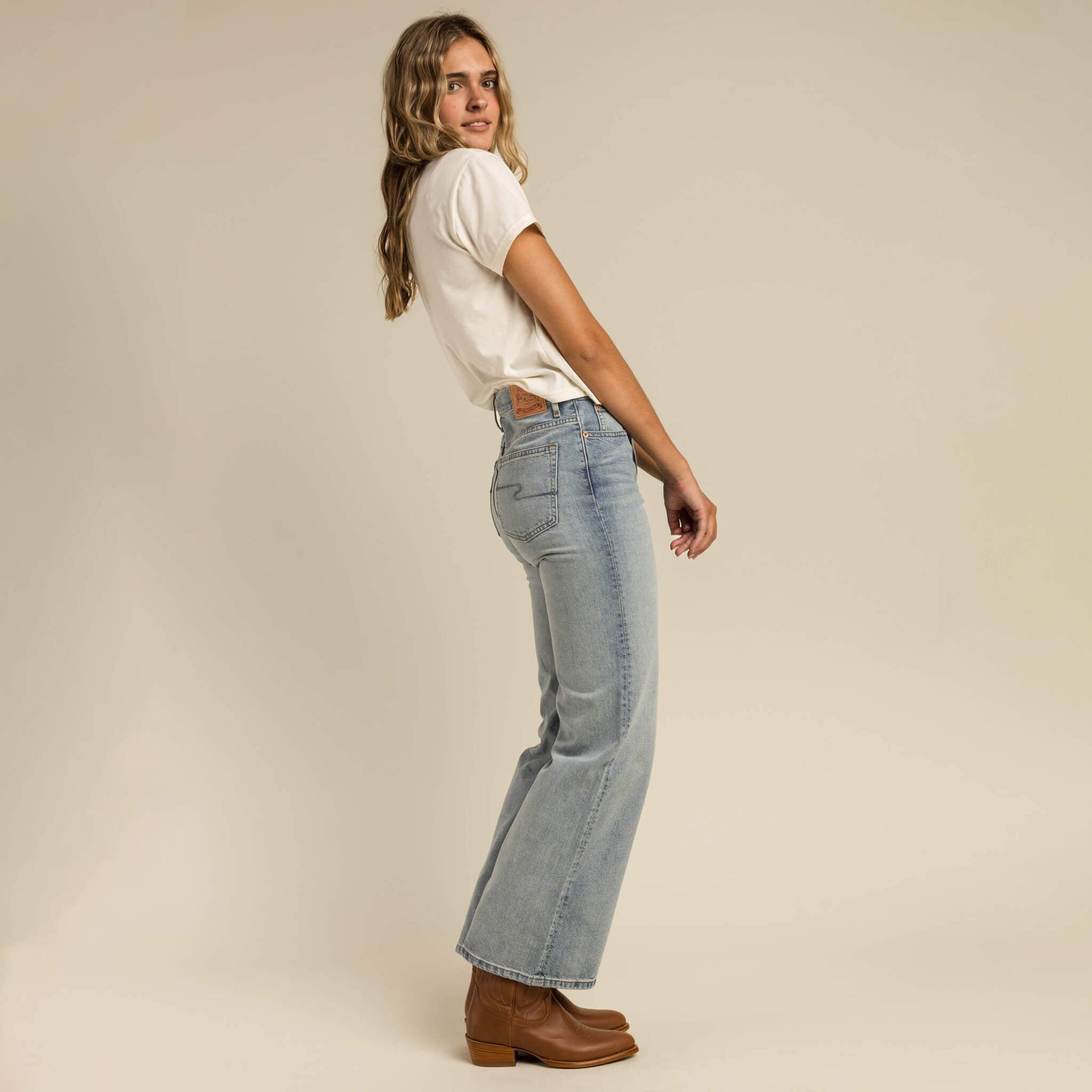 Woman wearing light blue jeans and a white shirt on a beige background