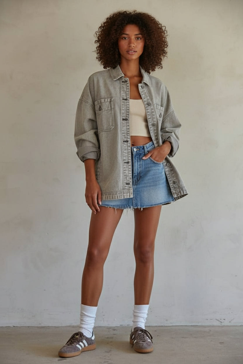 Woman wearing a denim jacket, beige top, and denim shorts against a plain background