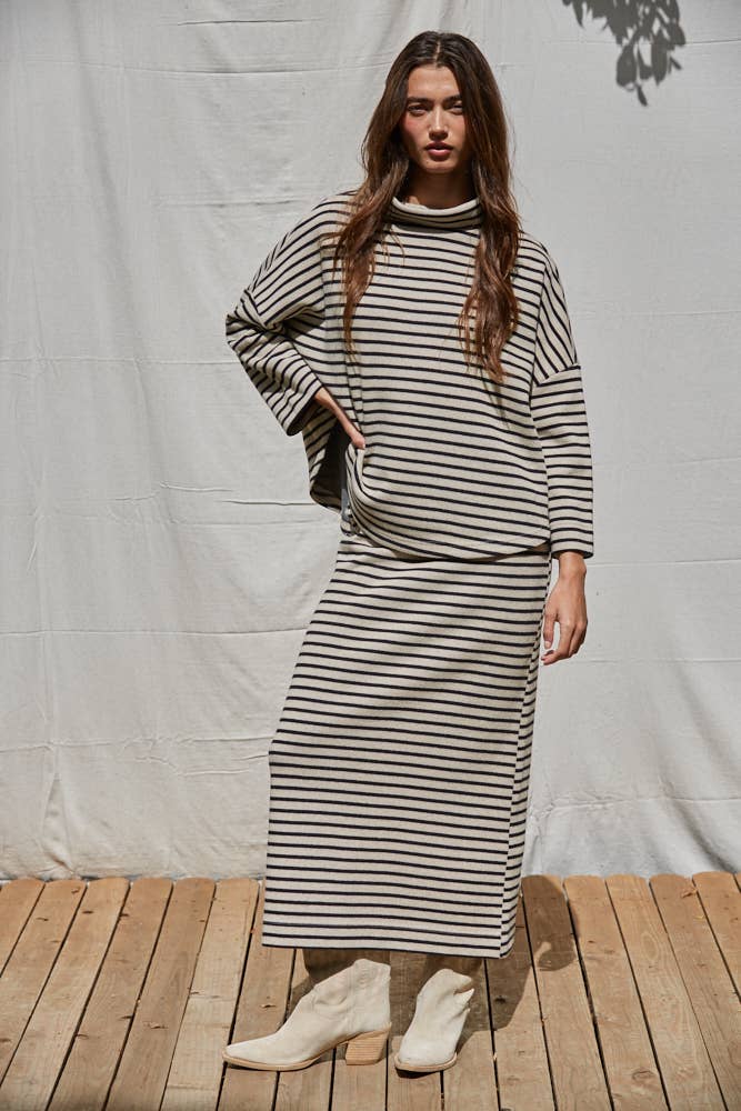 Woman wearing a black and white striped dress standing on a wooden floor with a white curtain background