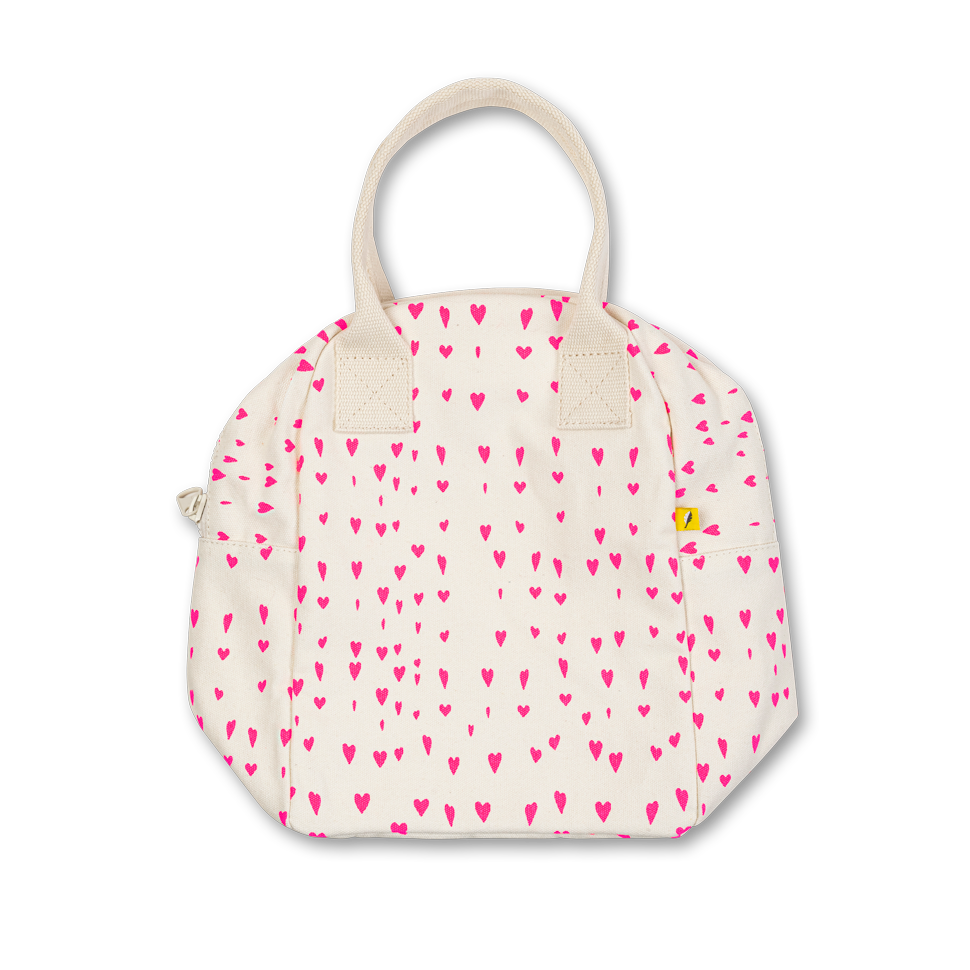 An off-white canvas lunch bag with a pattern of small pink hearts, featuring cream-colored handles and a small yellow brand tag on the side pocket.