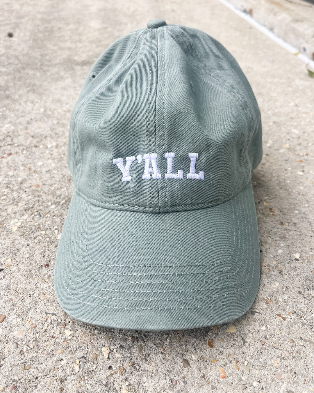Green cap with 'Y'ALL' text on a concrete surface