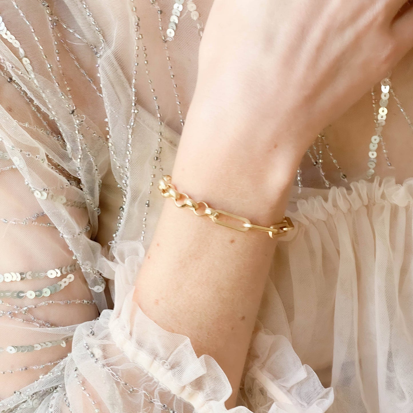 Gold bracelet on a wrist with a light, textured fabric background