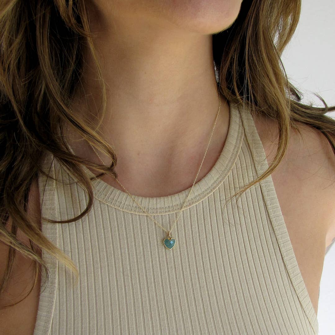 Close-up of a person wearing a gold necklace with a heart-shaped pendant.