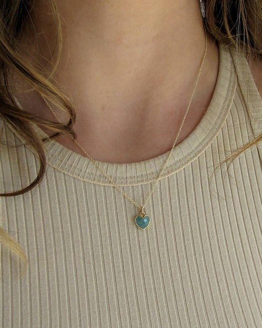 Close-up of a person wearing a gold necklace with a heart-shaped pendant.