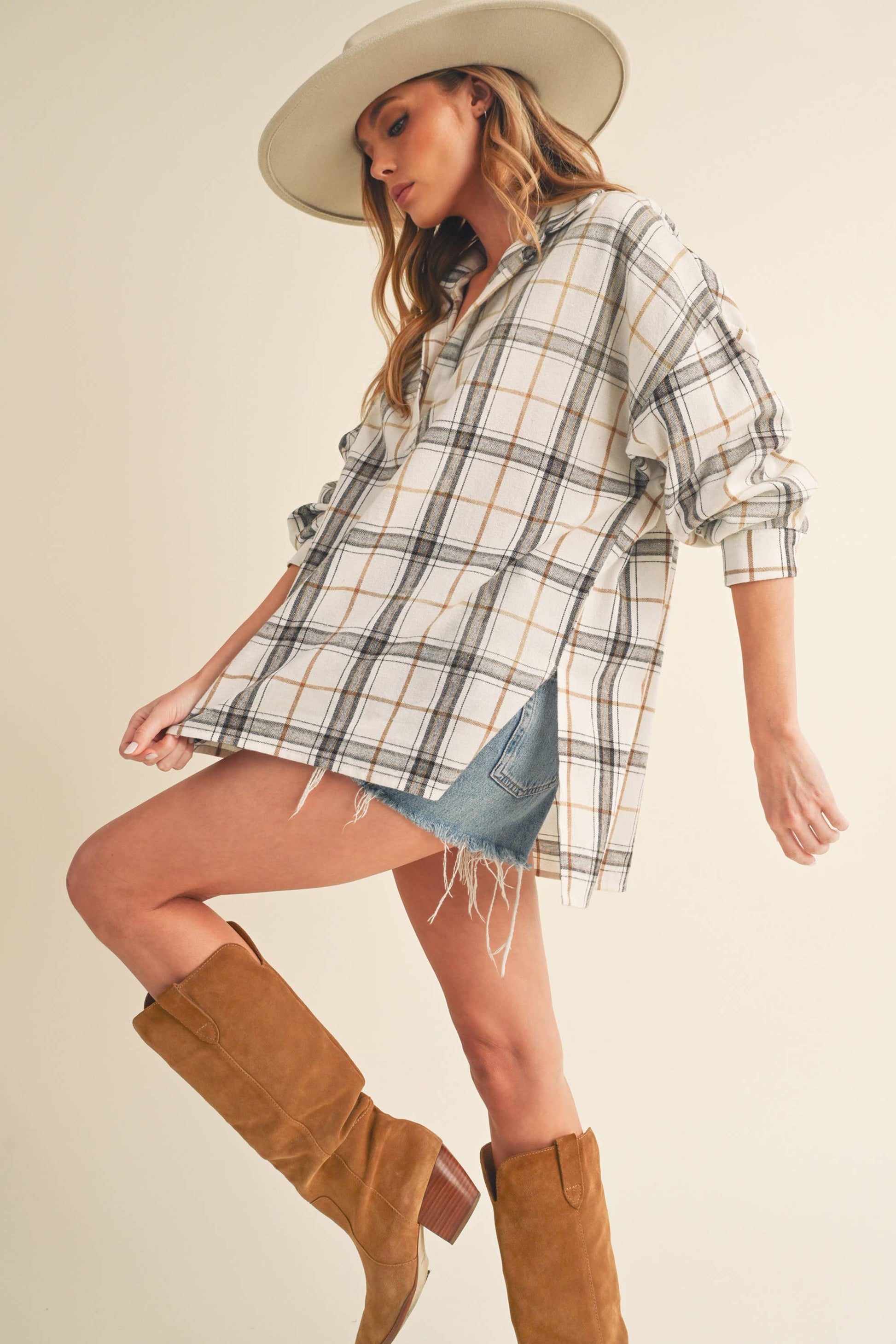 Woman wearing a plaid shirt, denim shorts, and brown boots on a beige background