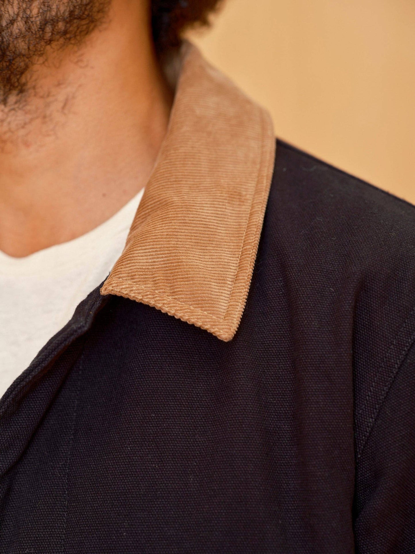 Close-up of a person wearing a dark jacket with a brown collar against a beige background