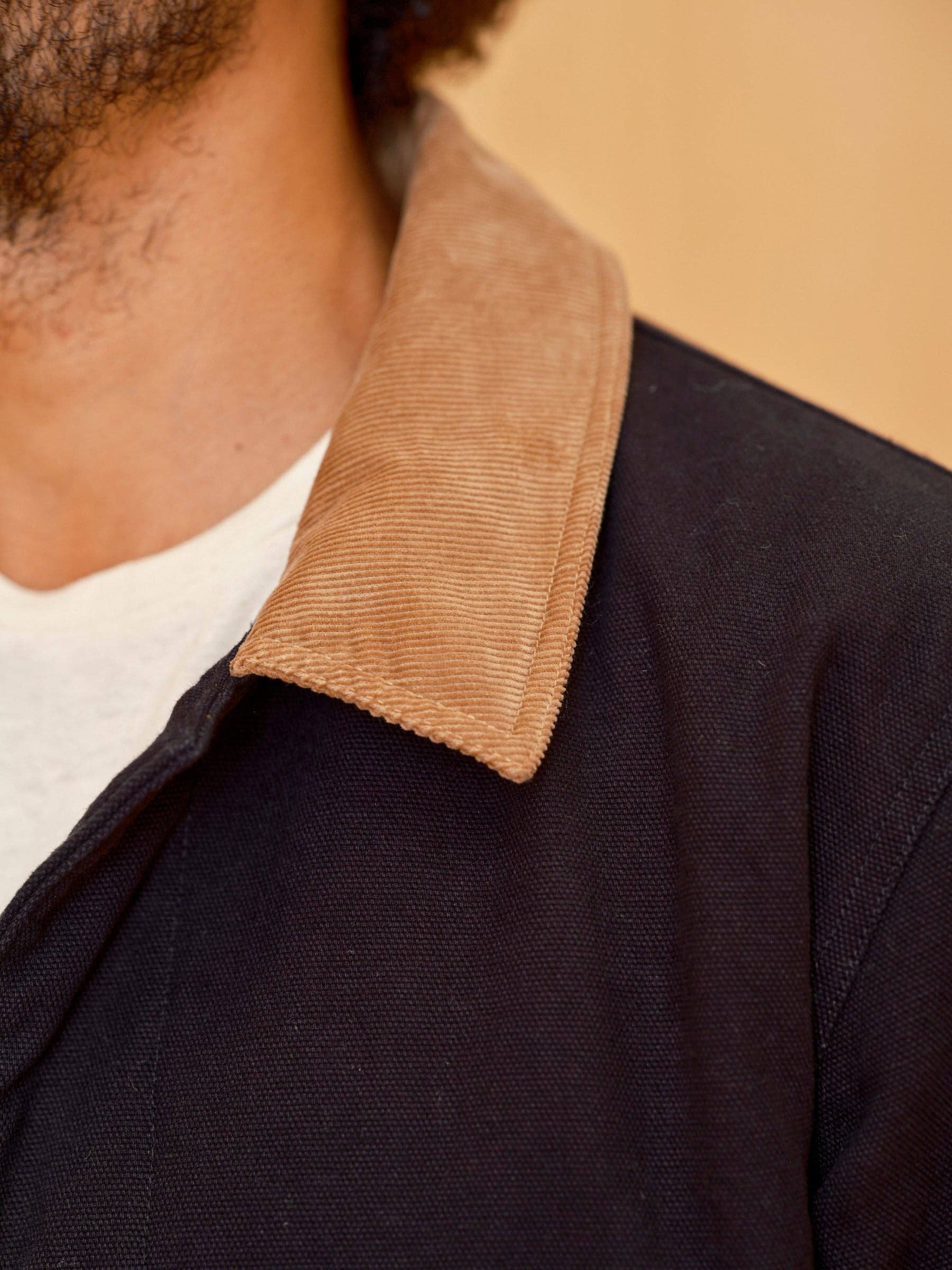 Close-up of a person wearing a dark jacket with a brown collar against a beige background
