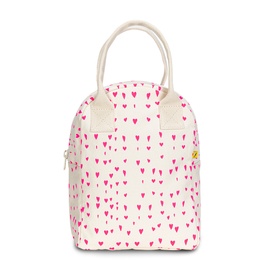 An off-white canvas lunch bag with a repeating pattern of small pink hearts, featuring cream-colored rope handles and a small yellow brand tag on the right side.