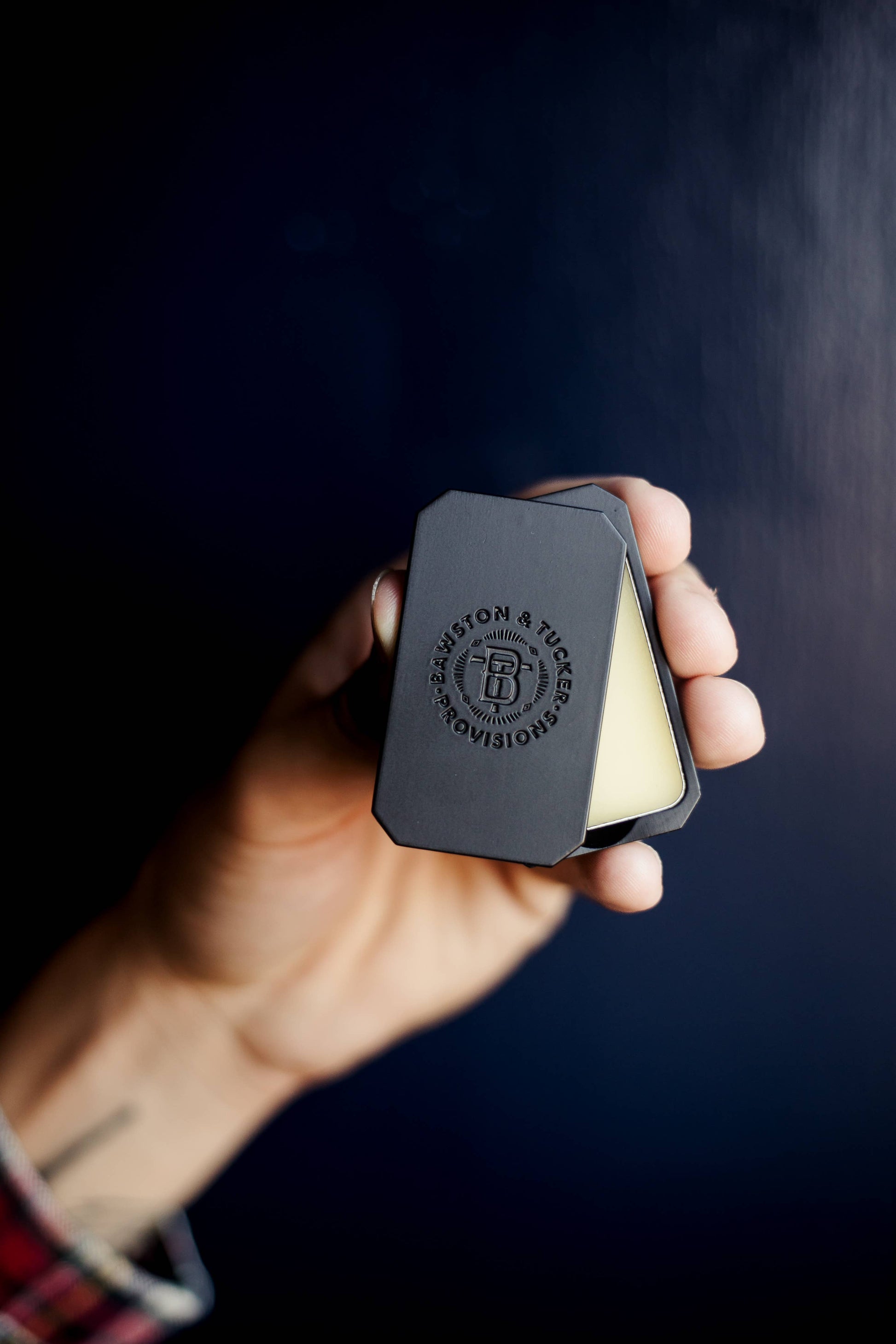 Hand holding a black case with a visible brand logo against a dark background