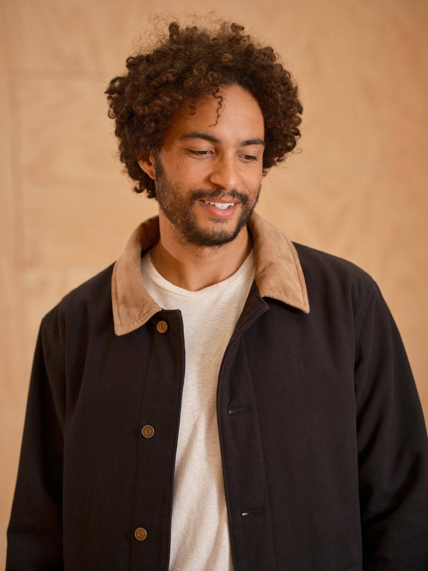Man wearing a dark jacket with a beige collar against a beige background