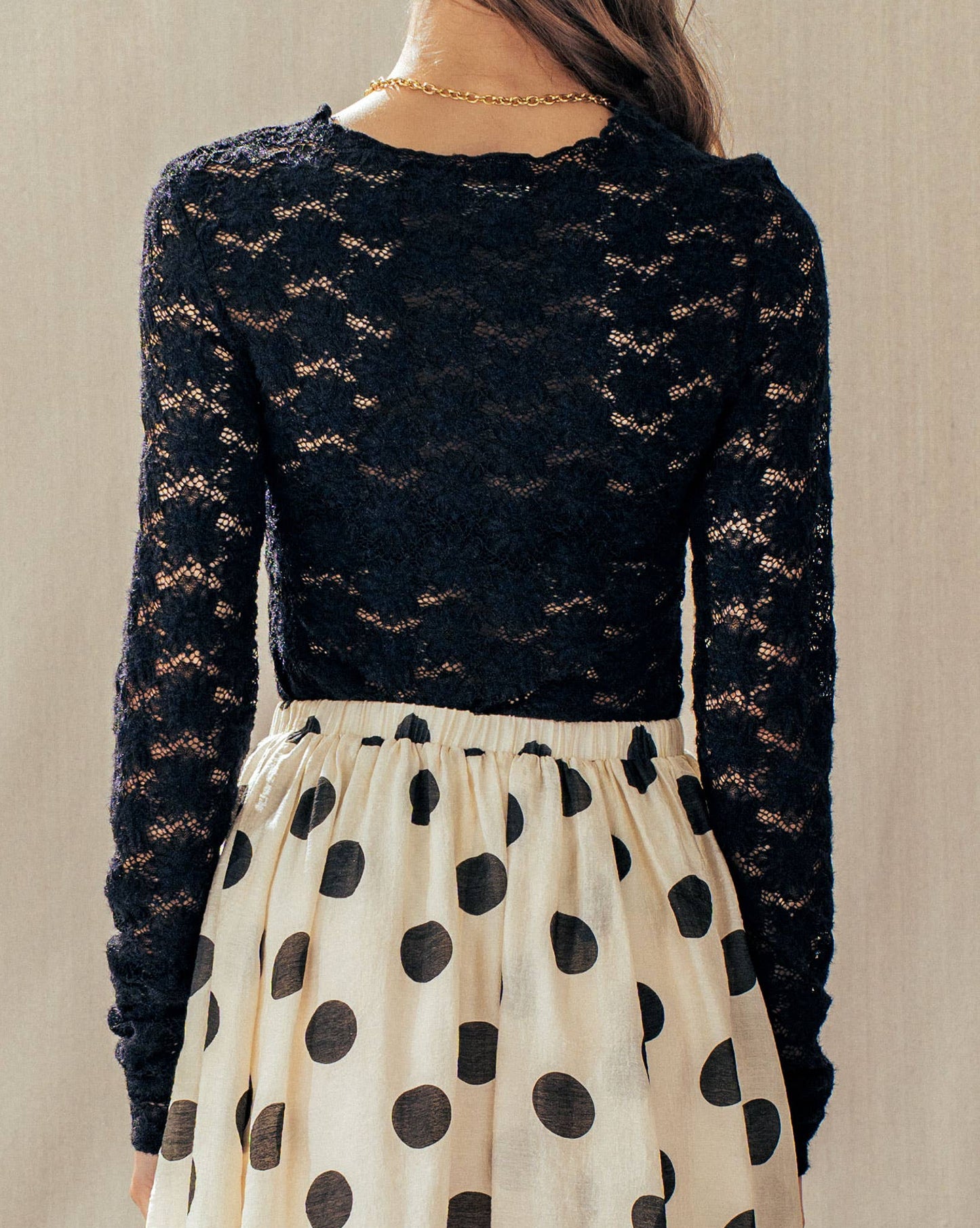 Person wearing a black lace top and polka dot skirt against a neutral background