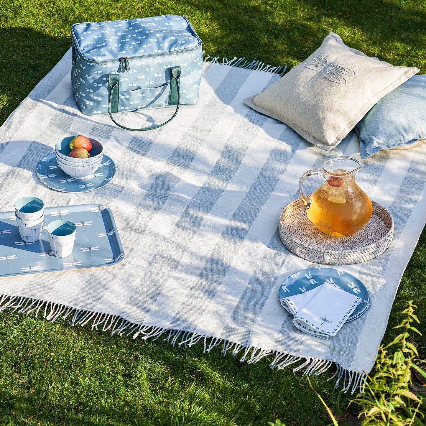 Picnic setup on a checkered blanket with a cooler bag, pillows, and tableware.