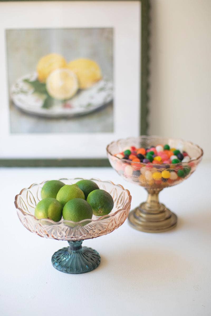 Two glass bowls, one with green limes and the other with colorful candies, on a white surface.