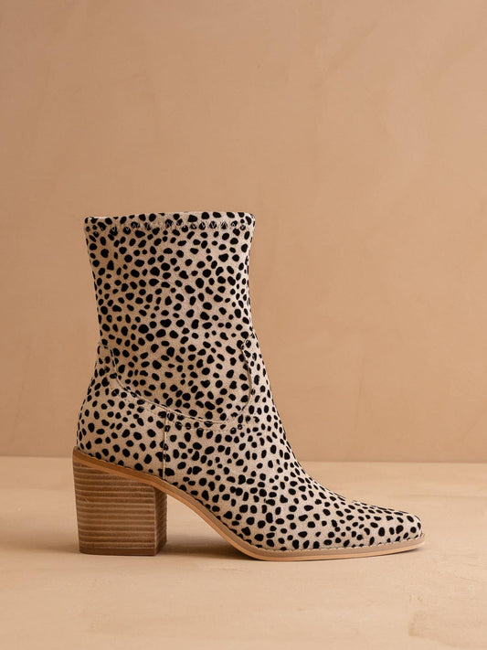 A single ankle boot with a black-on-beige animal print, featuring a stacked wooden-look block heel and a pointed toe, set against a solid beige background.