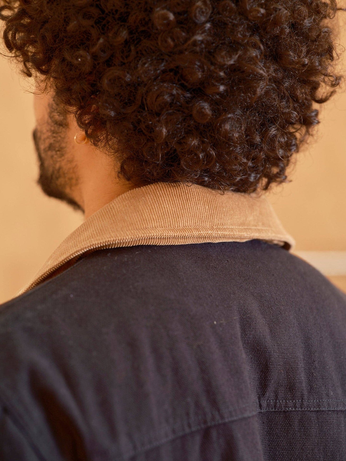 Person wearing a dark jacket with a beige collar against a beige wall