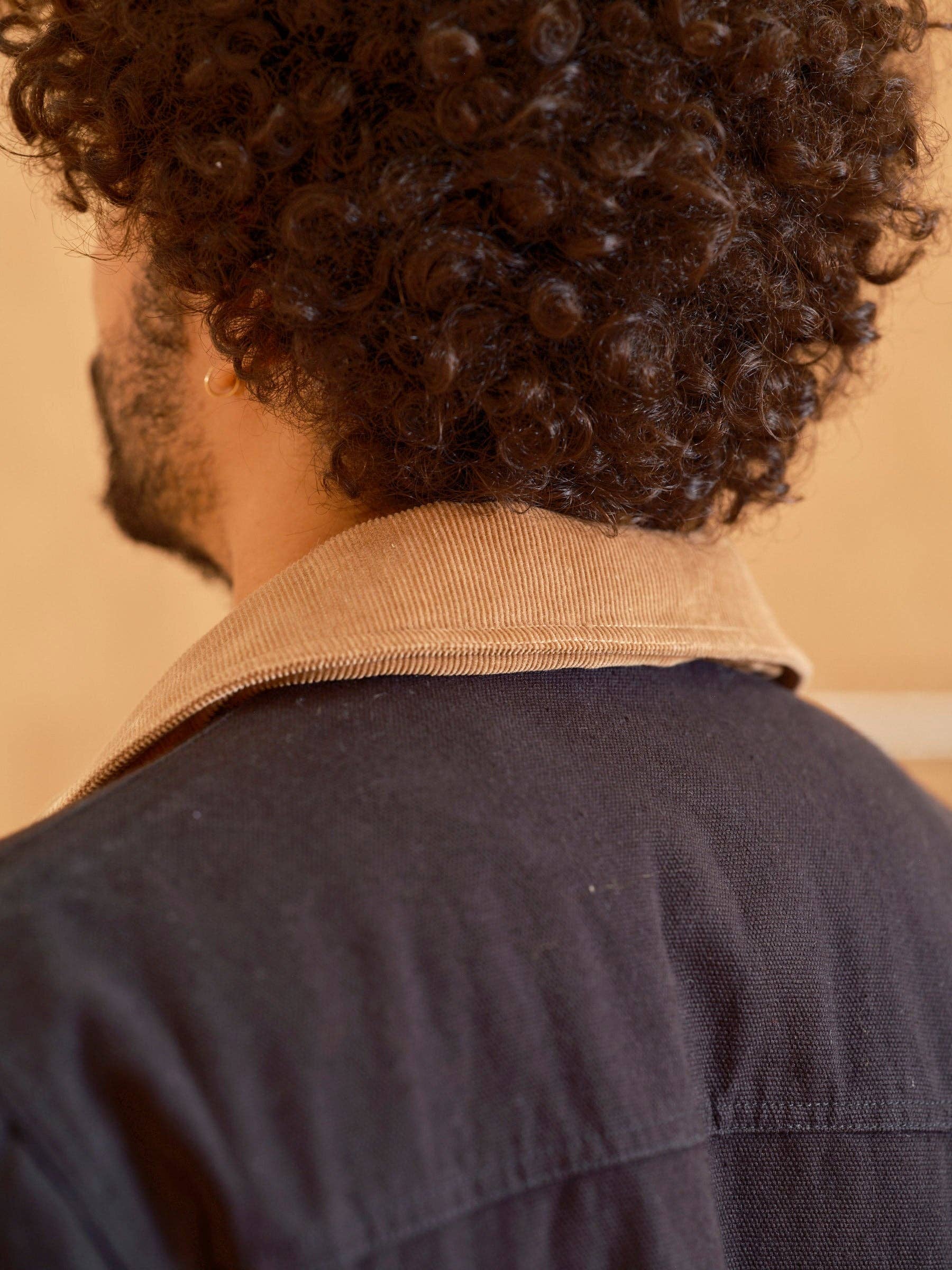 Person wearing a dark jacket with a beige collar against a beige wall