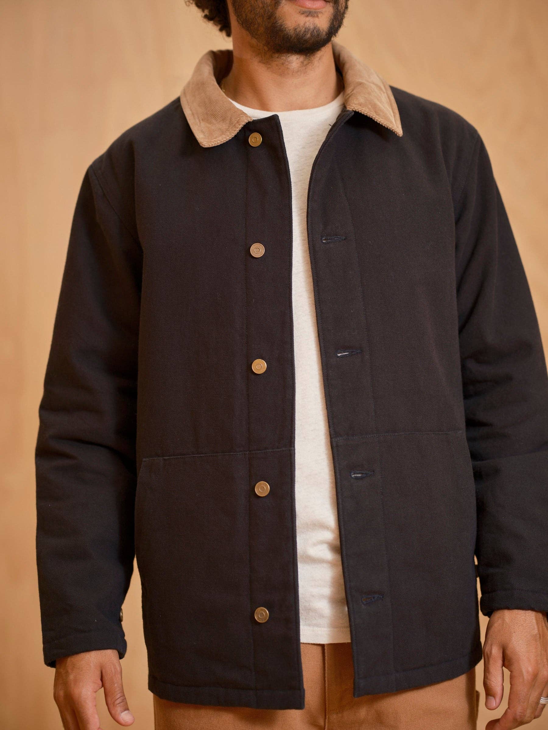 Man wearing a black jacket with a beige collar against a beige background