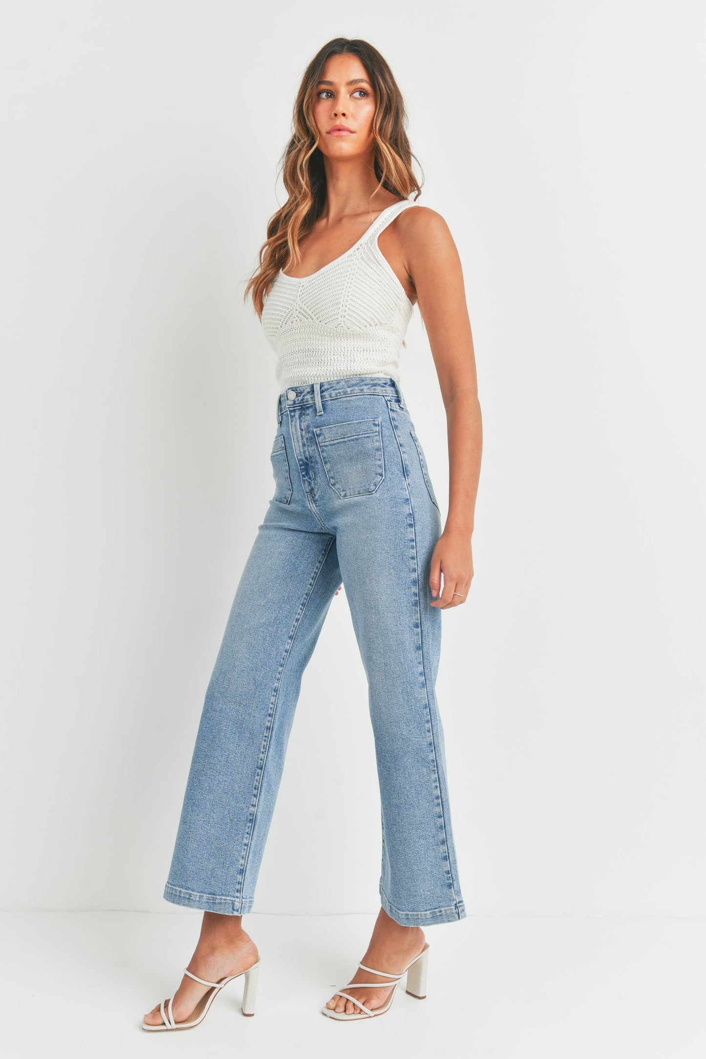 Woman wearing a white sleeveless top and light blue jeans on a white background