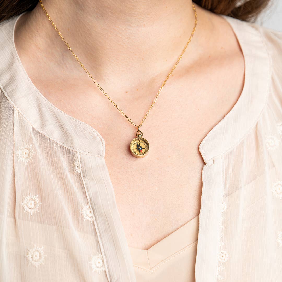 Gold necklace with a pendant worn by a person in a light blouse