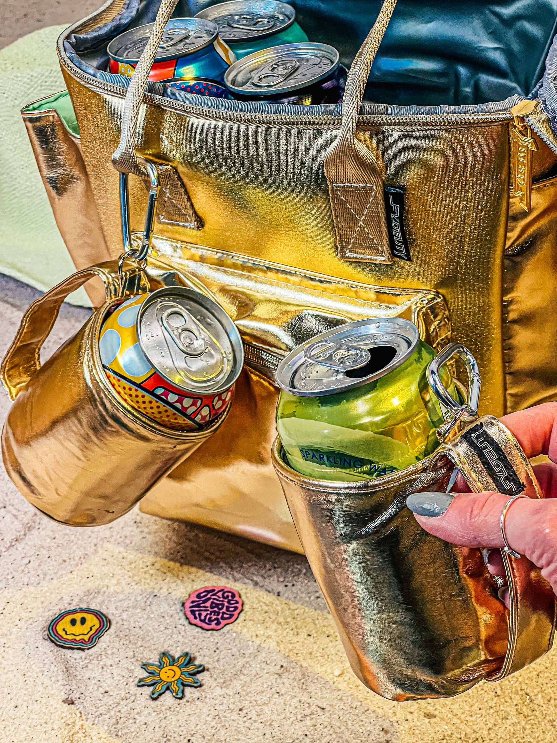 Gold insulated beverage holder with cans and a cooler bag on a textured surface.