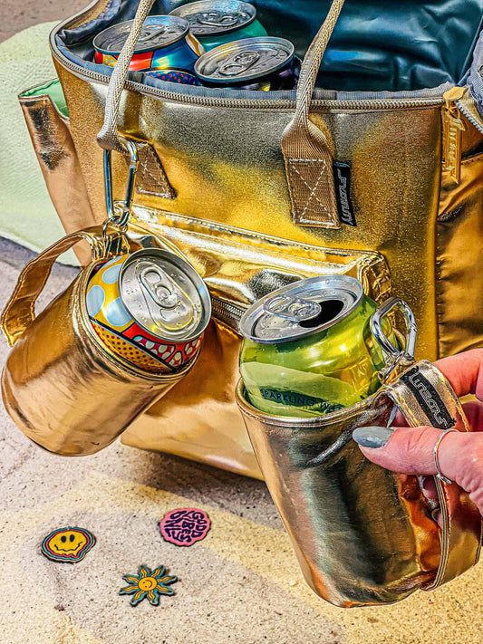 Gold insulated beverage holder with cans and a cooler bag on a textured surface.