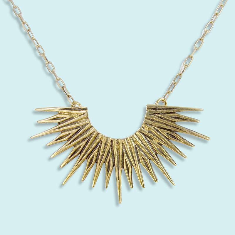Gold necklace with a sunburst design on a light blue background