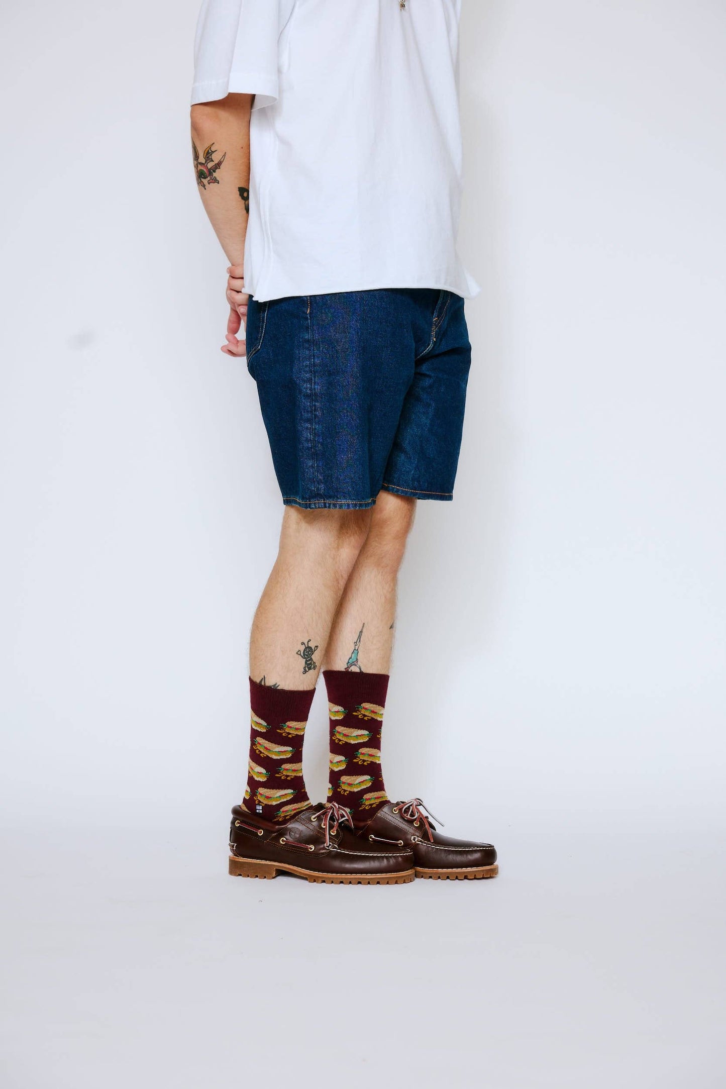 Person wearing blue shorts, white shirt, brown shoes, and patterned socks on a plain background