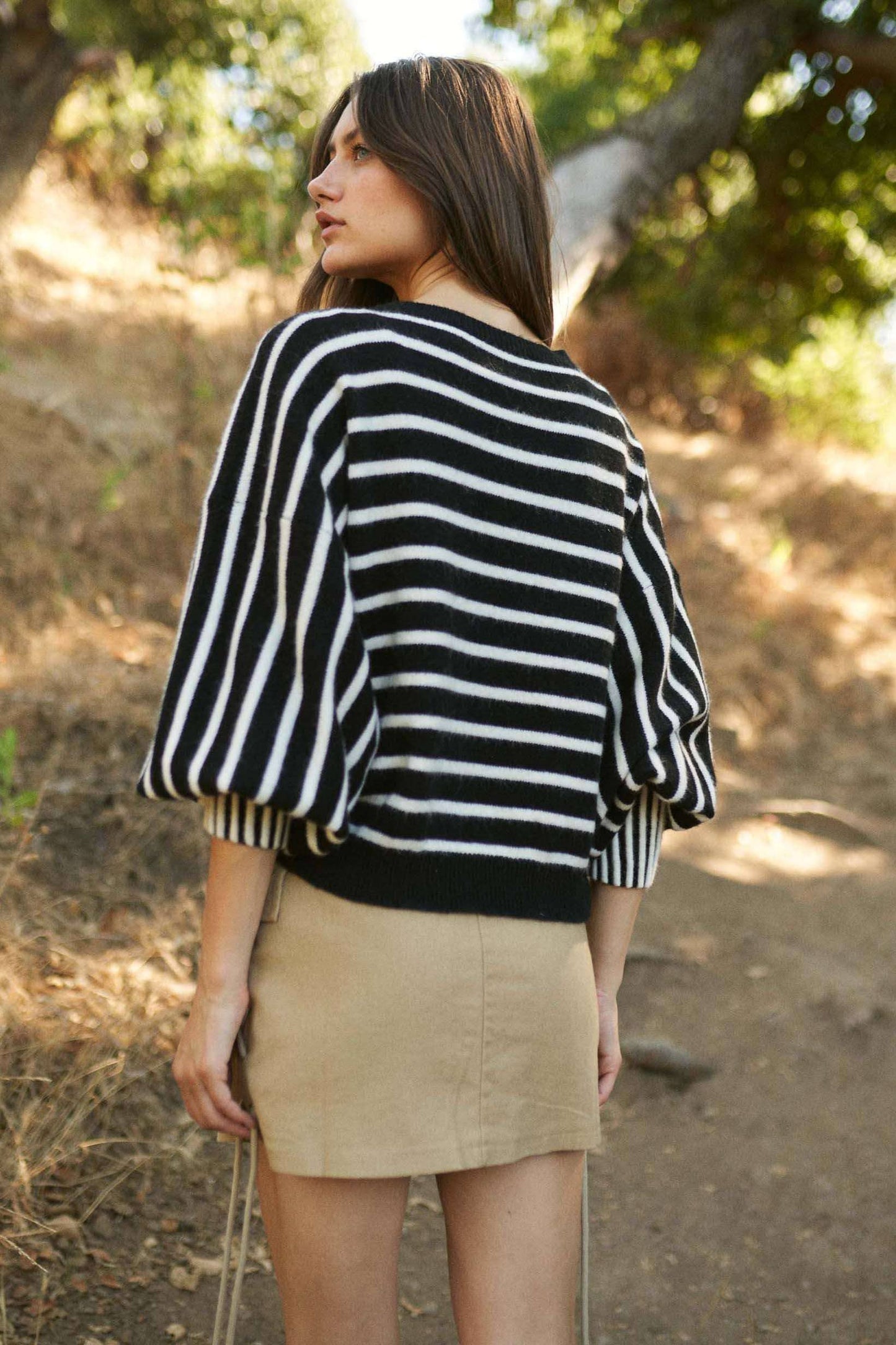 Woman wearing a black and white striped sweater and beige skirt outdoors.