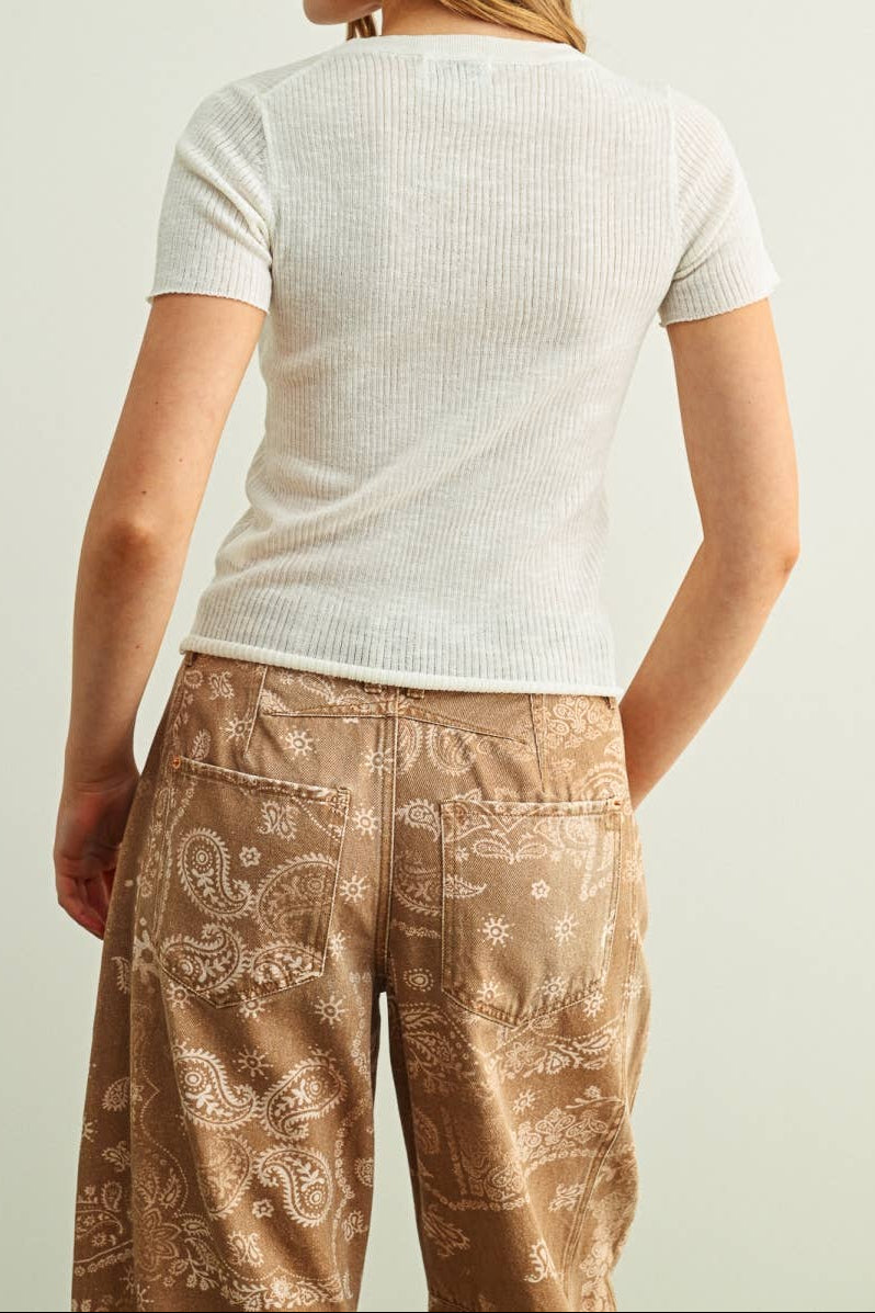 Woman wearing a white top and patterned brown pants on a plain background
