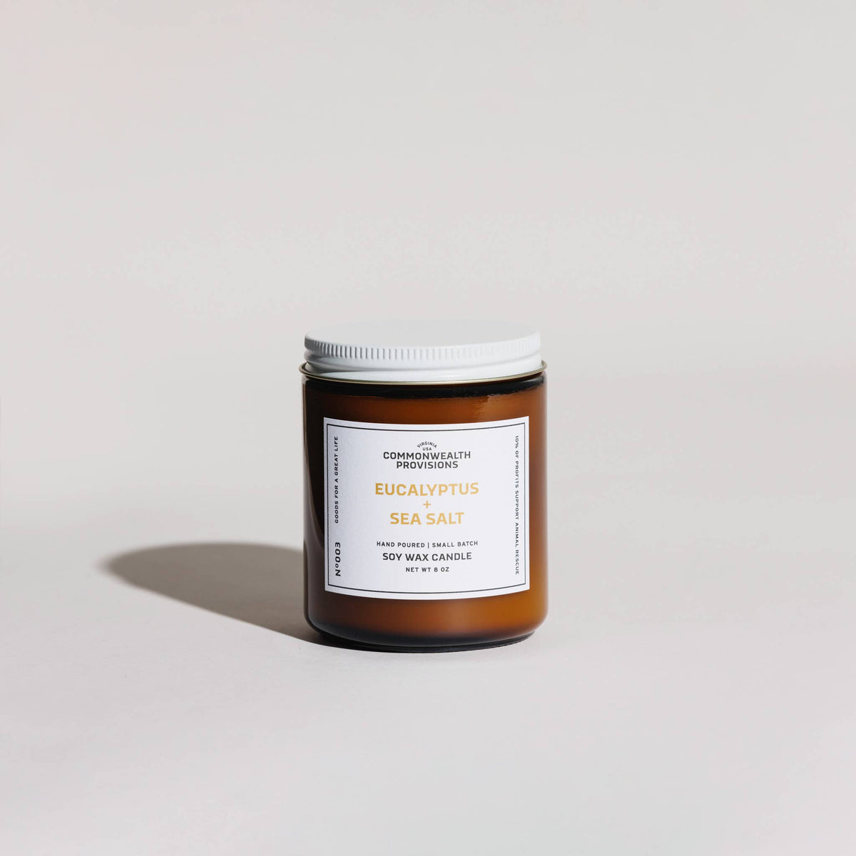 An amber glass jar candle with a white lid and a white label reading 'EUCALYPTUS SEA SALT' by Commonwealth Provvisions, photographed on a clean light gray studio background.