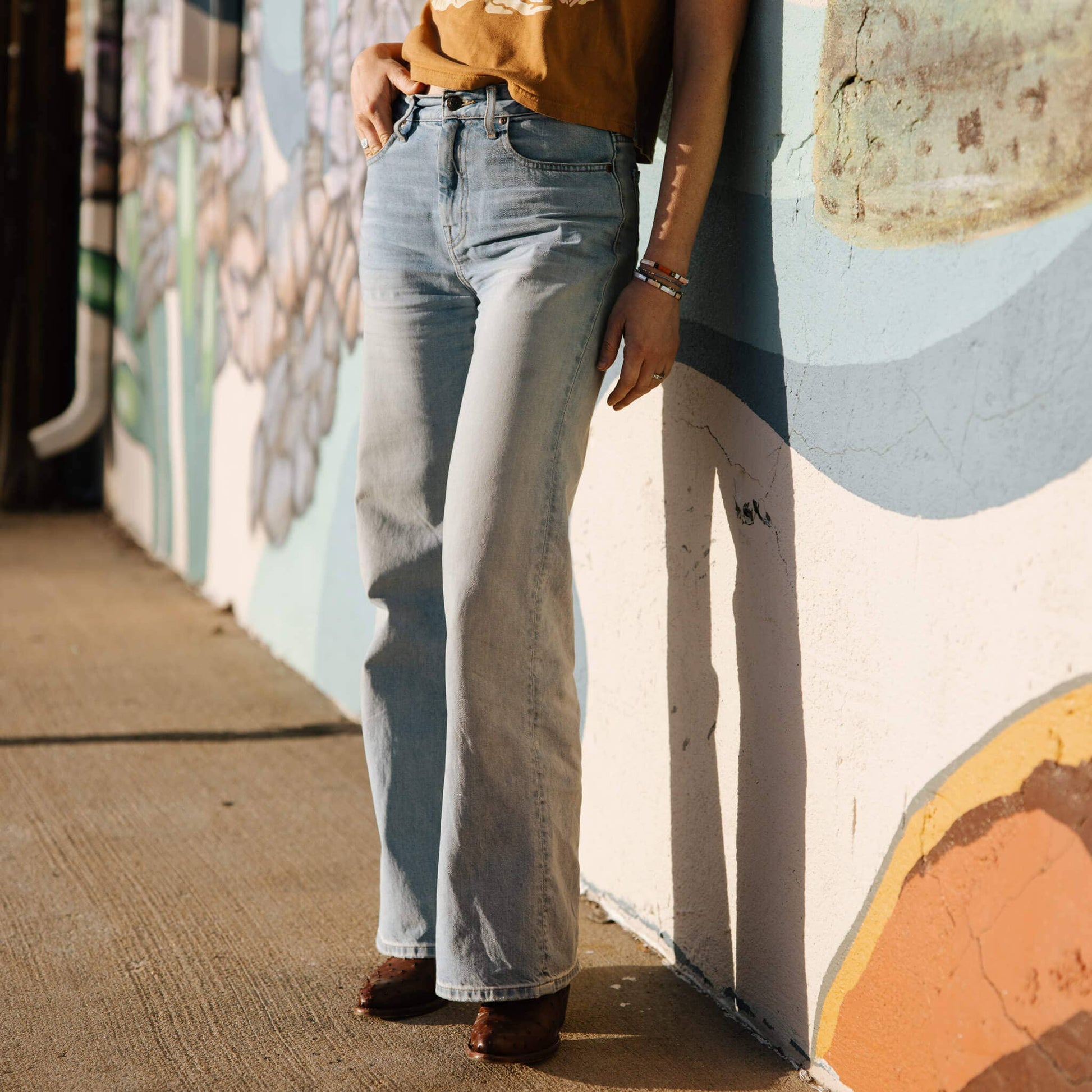 Person wearing light blue jeans standing against a colorful mural.
