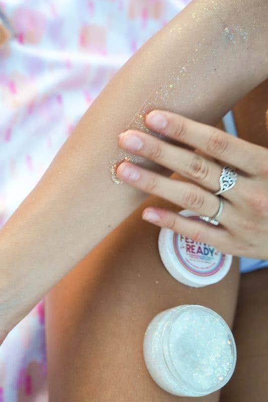 Person applying a white cream or lotion to their arm with a pink and white blurred background.