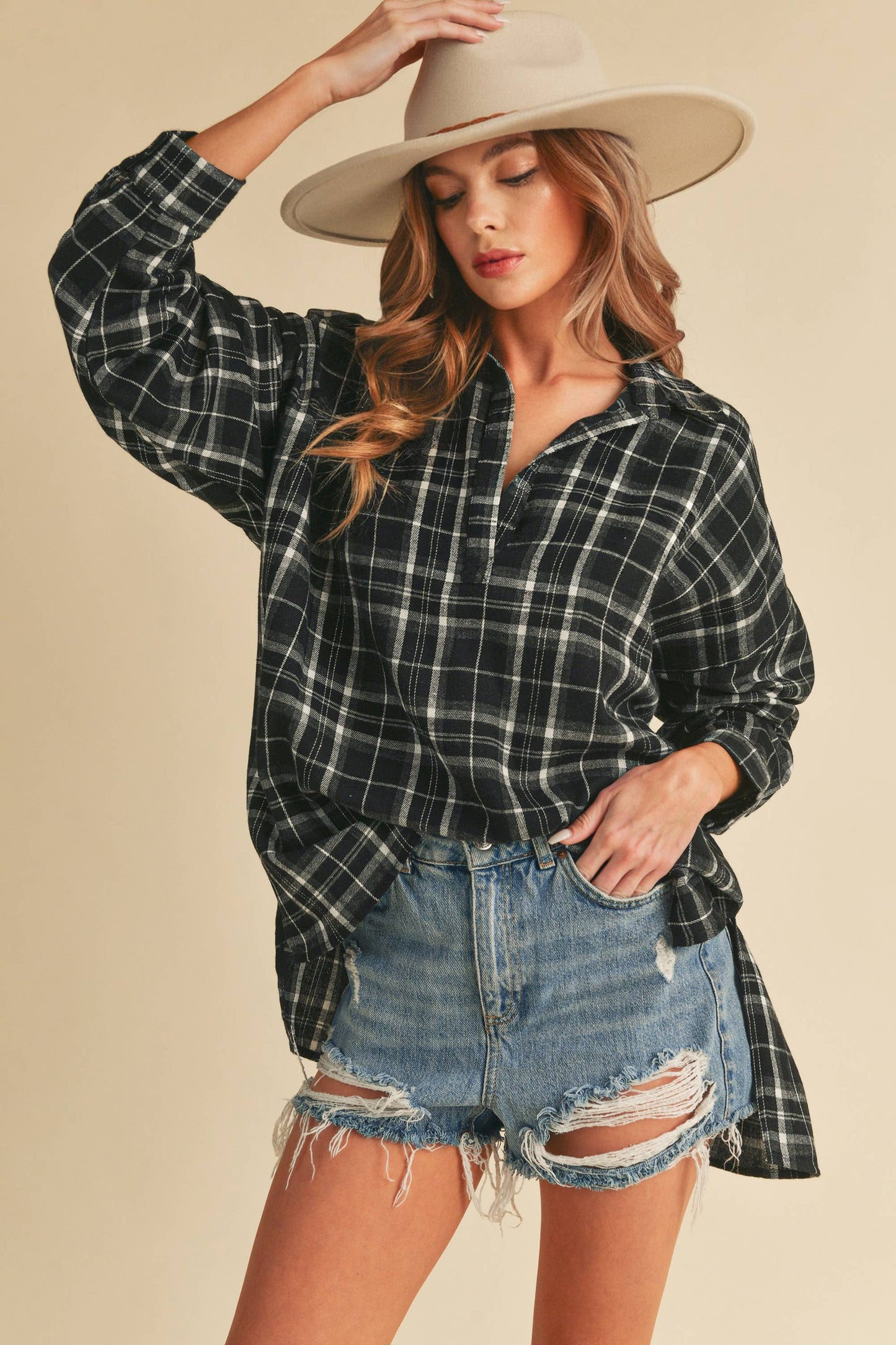 Woman wearing a plaid shirt, denim shorts, and a beige hat on a beige background