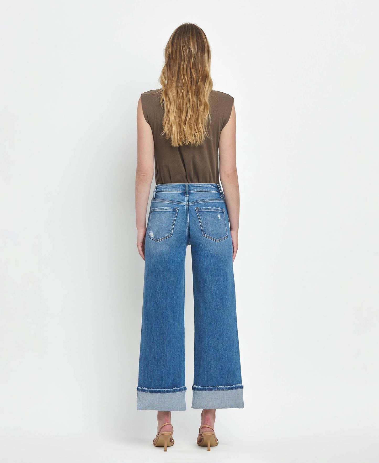 Person wearing blue jeans and a brown top on a white background
