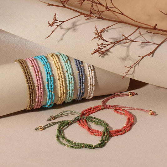 Set of beaded bracelets in various colors on a beige surface with dried branches.
