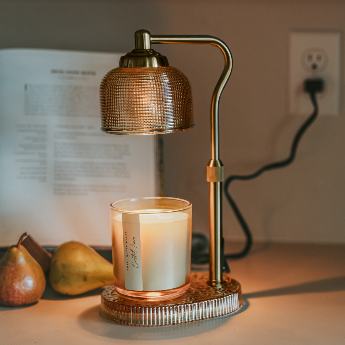 Decorative lamp with a candle on a table next to pears and a blurred book