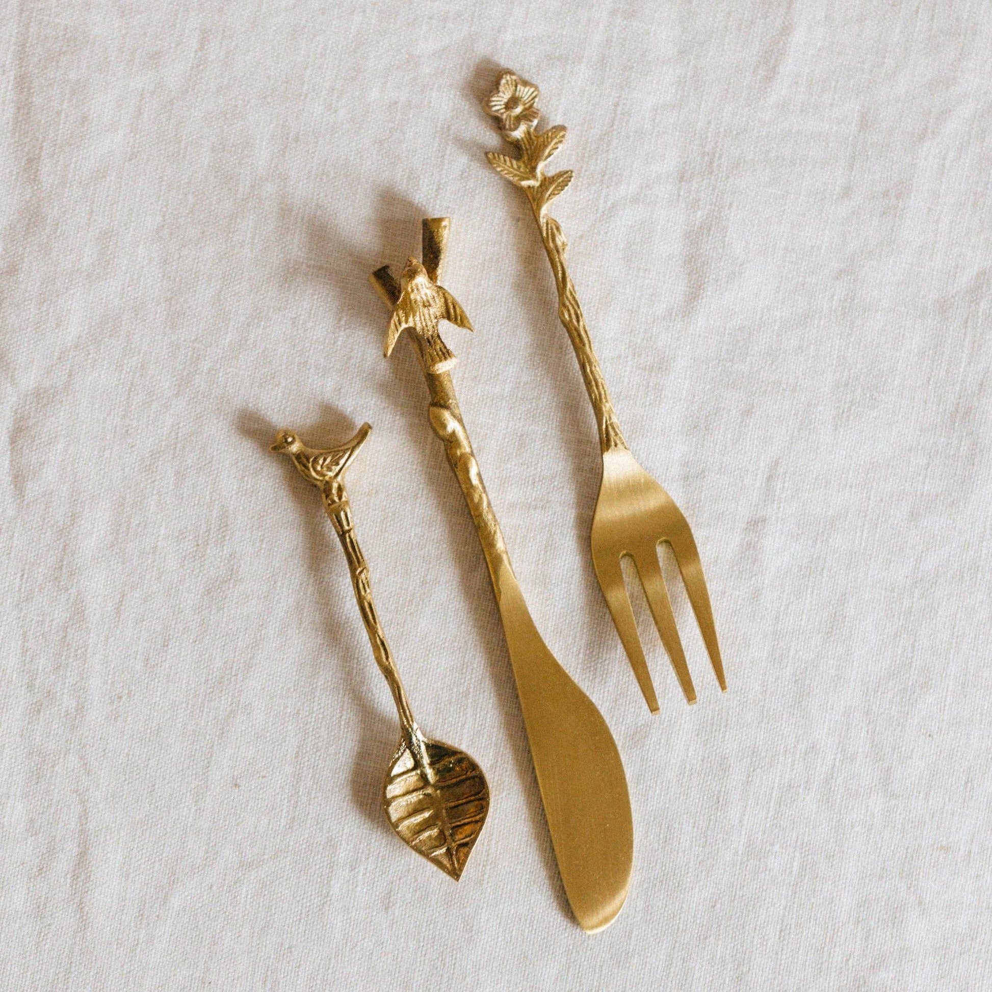 Set of gold cutlery with decorative handles on a white fabric background