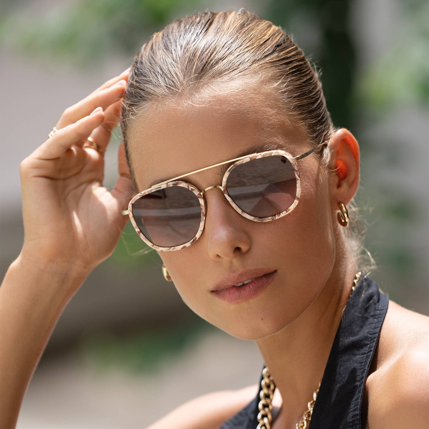 Woman wearing gold-framed sunglasses with a blurred outdoor background