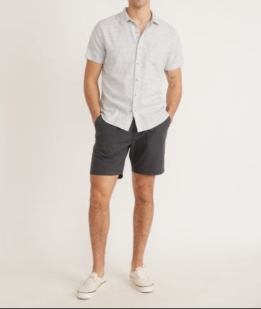 Man wearing a light gray short-sleeve shirt and dark gray shorts on a white background