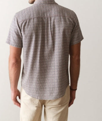 Man wearing a checkered shirt and beige pants against a plain background