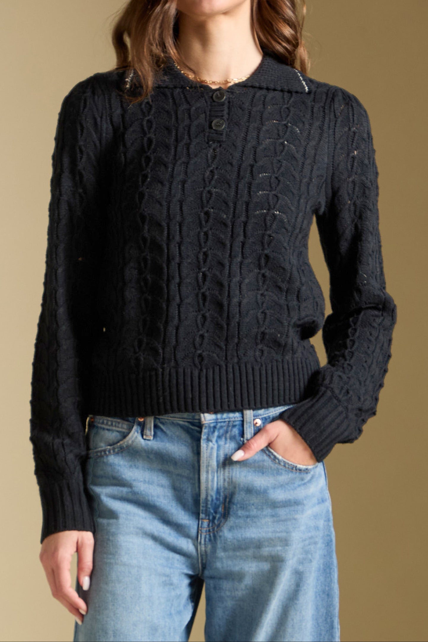 Woman wearing a black cable knit sweater and blue jeans against a beige background