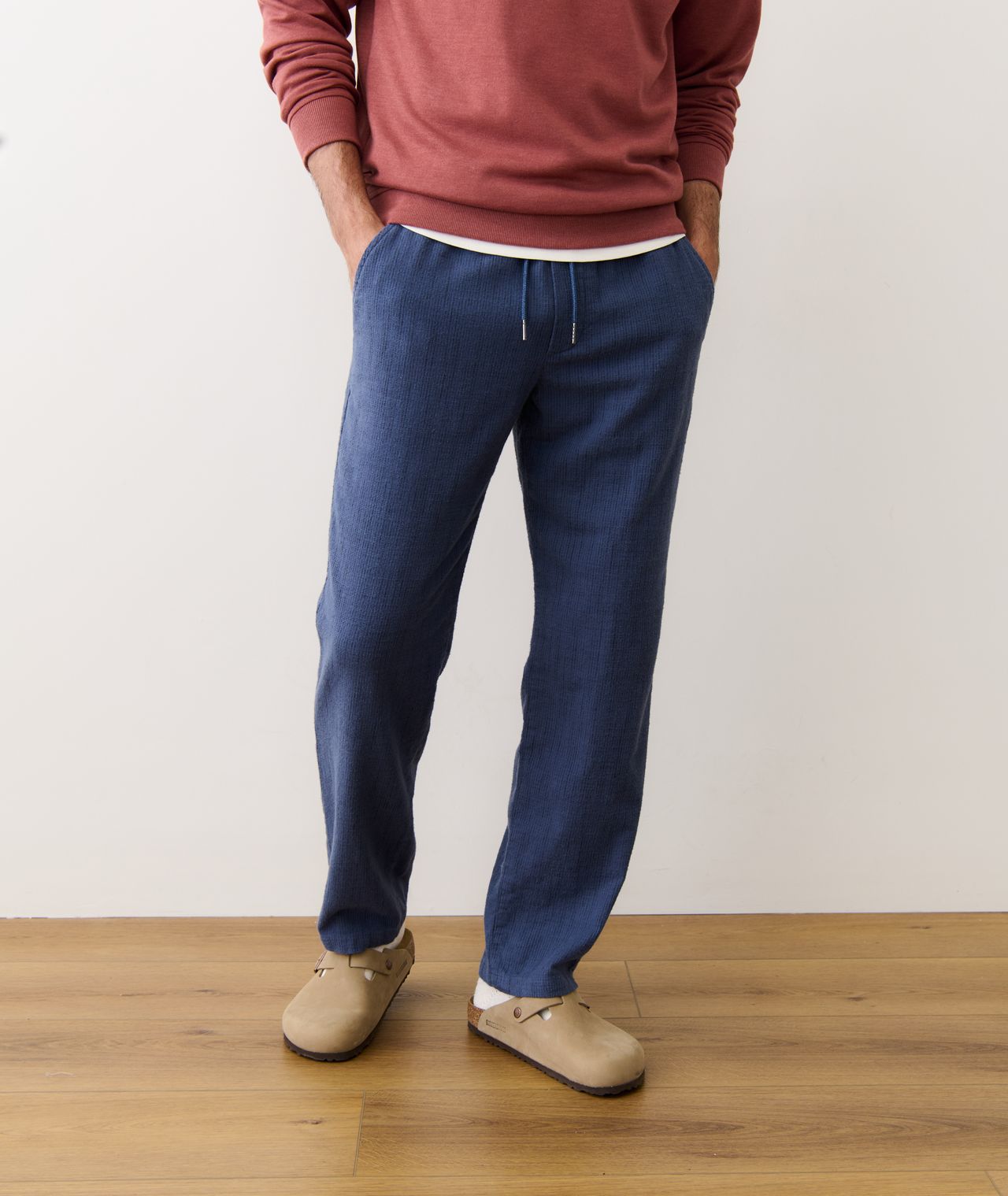 Person wearing a red sweater and blue pants standing on a wooden floor with a white wall background