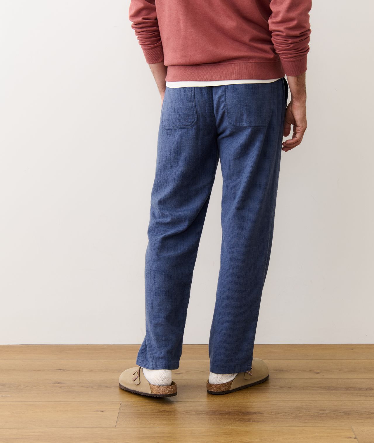 Person wearing blue pants and a red sweater on a wooden floor with a white wall background