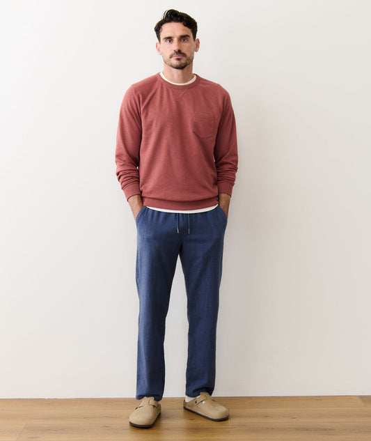 Man wearing a red sweater and blue pants standing against a white wall.
