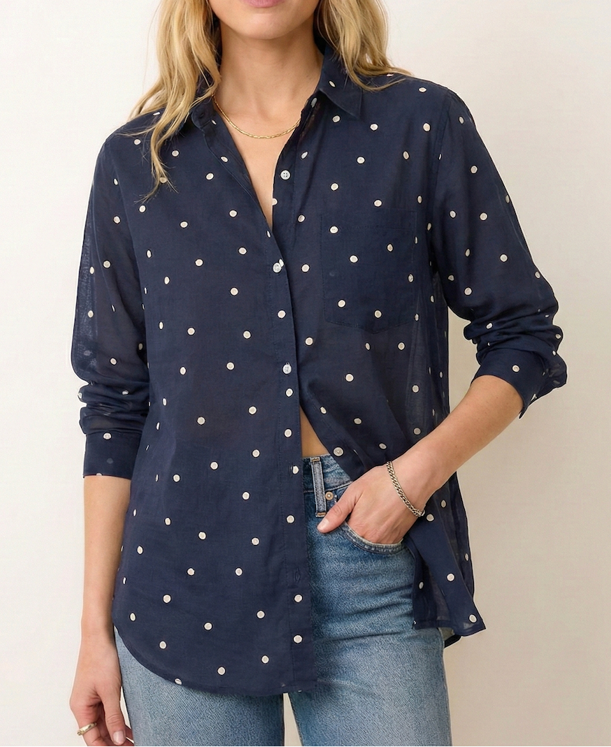 Woman wearing a navy blue shirt with white polka dots and jeans against a plain background