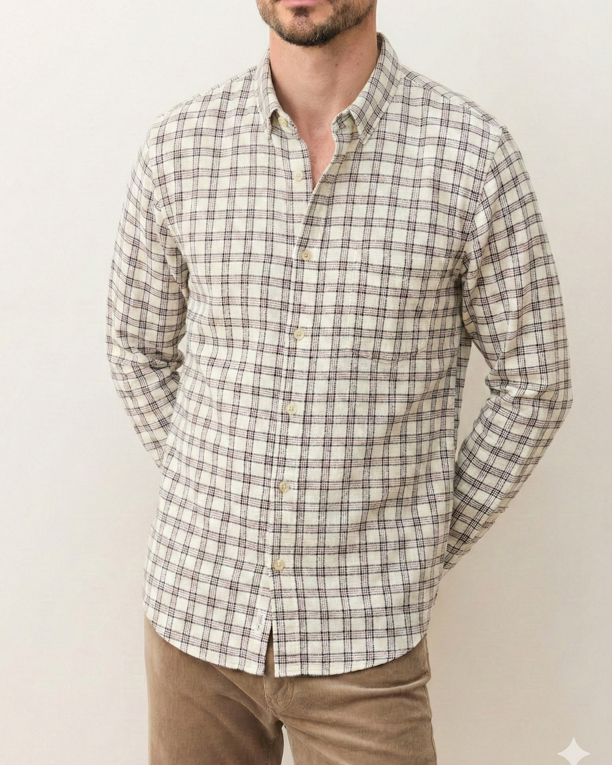 Man wearing a plaid shirt and beige pants against a plain background