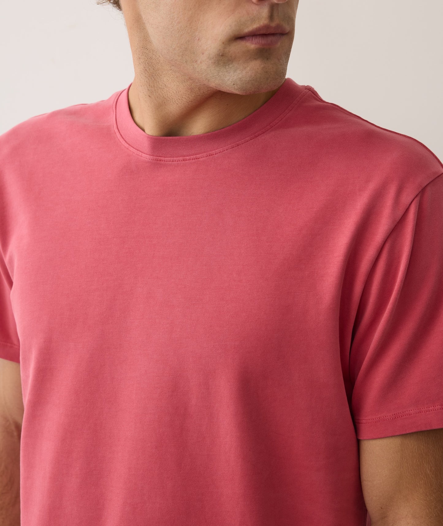 Close-up of a person wearing a plain pink t-shirt against a neutral background